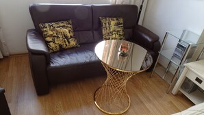 Un divano in pelle marrone scuro con cuscini a fantasia, un tavolino rotondo con base in filo d'oro e un elettrodomestico bianco sullo sfondo.