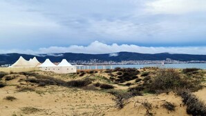 Paesaggio costiero con dune, spiaggia e una città sullo sfondo.