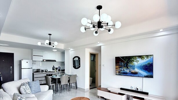 Una sala moderna con un sofá seccional, un comedor, una cocina y un televisor montado en la pared.