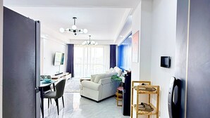 Una sala moderna con un sofá, una mesa de comedor y sillas, un zapatero de madera y una lámpara de techo.