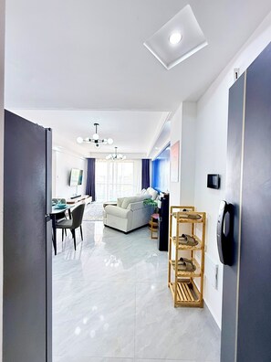 A modern living room with a sofa, dining table, and chairs, a wooden shoe rack, and a ceiling light. - Araka Homes-Westlands/Elegant 2 Bedroom Apartment (Nairobi)