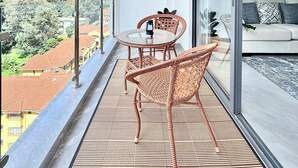 Un balcón con mesa y sillas, un sofá y vistas a edificios y árboles.