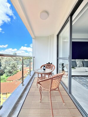 A balcony with a table and chairs, a sofa, and a view of buildings and trees. - Araka Homes-Westlands/Elegant 2 Bedroom Apartment (Nairobi)
