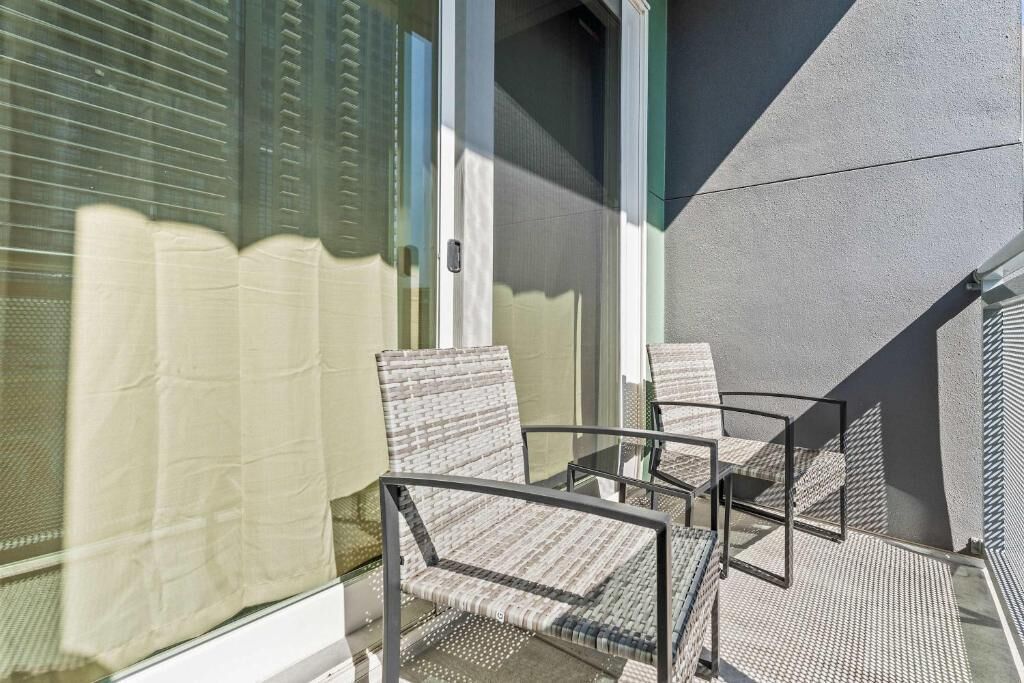A balcony with two chairs, a glass door, and a textured wall.