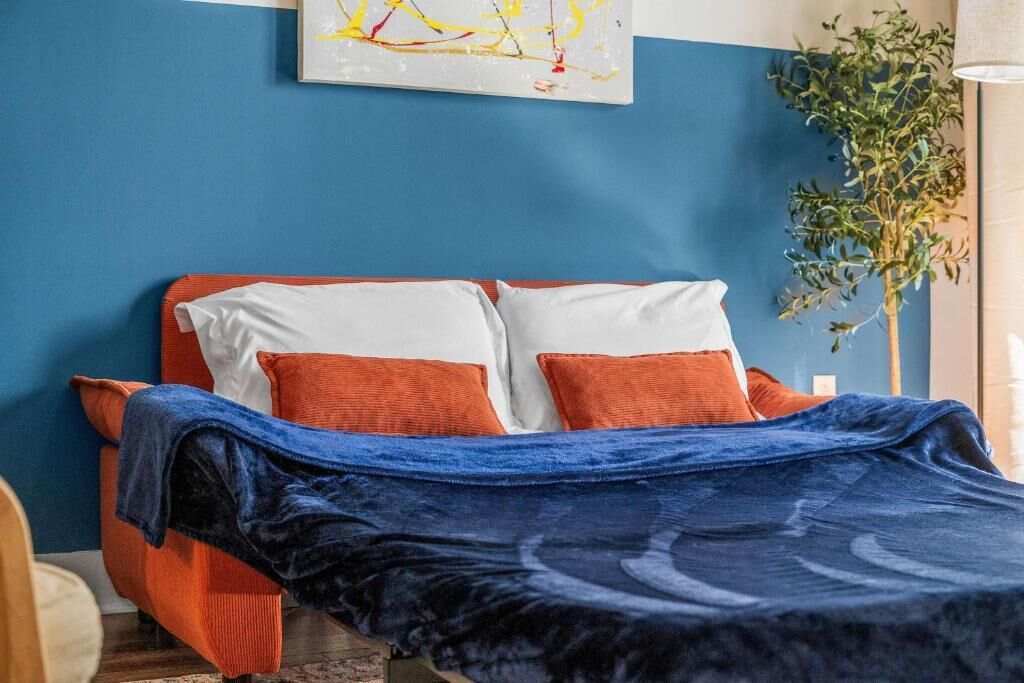 A bed with a blue blanket, orange pillows, and a white headboard.