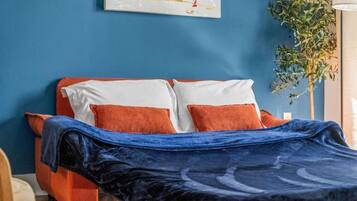 A bed with a blue blanket, orange pillows, and a white headboard.