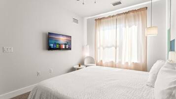 A hotel room with a bed, a TV mounted on the wall, a ceiling fan, and a window with curtains.