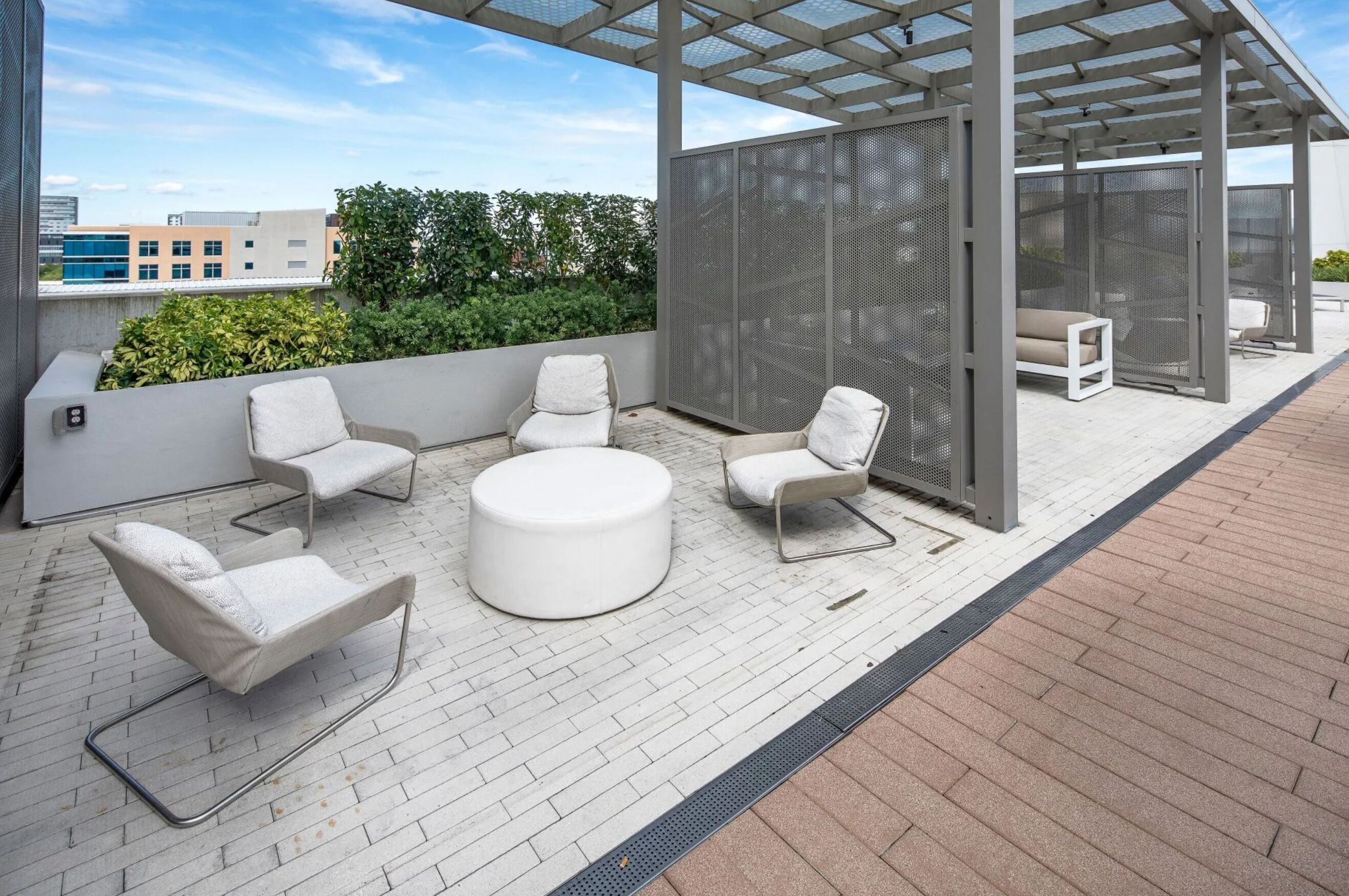 A rooftop terrace with outdoor seating, a pergola, and a view of buildings and greenery.