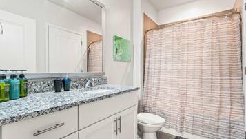 A bathroom with a white toilet, a shower curtain, and a granite countertop with toiletries.
