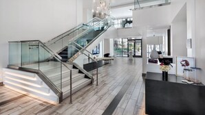 Un moderno vestíbulo de hotel con una escalera de cristal, una recepción y vistas al exterior.