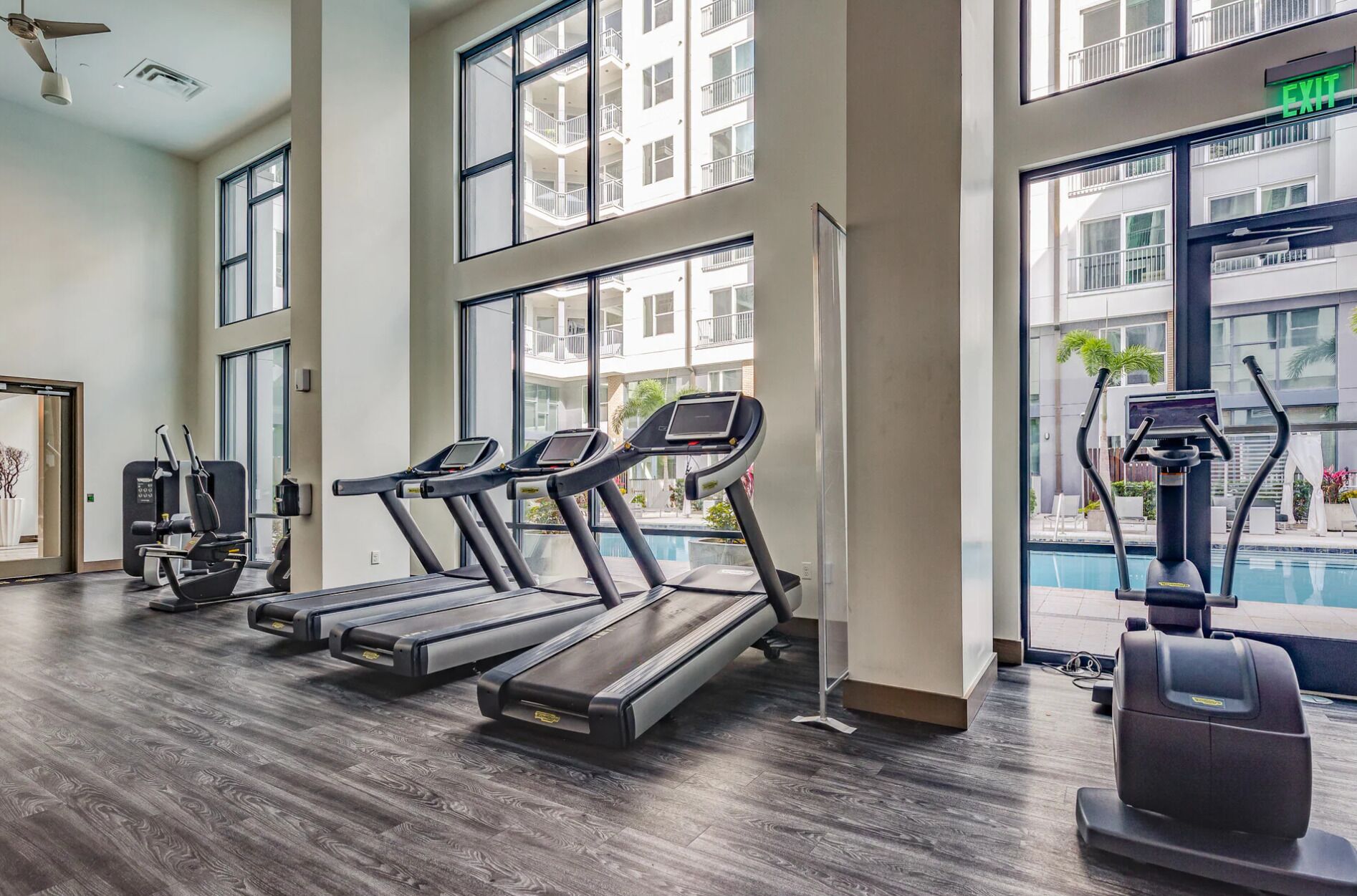 A gym with treadmills, exercise machines, and a view of a building with balconies.