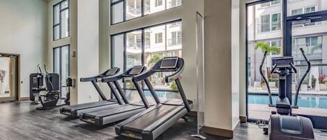 A gym with treadmills, exercise machines, and a view of a building with balconies.