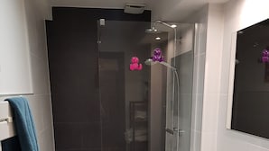Casa de banho moderna com cabine de duche em vidro, lavatório branco com espelho e um porta-toalhas com toalha azul.