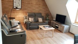 Uma sala de estar moderna com sofá, poltronas, mesa de centro, televisão e parede de madeira.