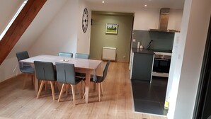 Uma área de refeições com mesa e cadeiras, uma cozinha com eletrodomésticos modernos e vista para o exterior.