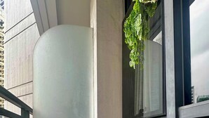 Ein Balkon mit gepolstertem Stuhl, einem gewebten Tablett mit Dekoration und einer hängenden Pflanze.