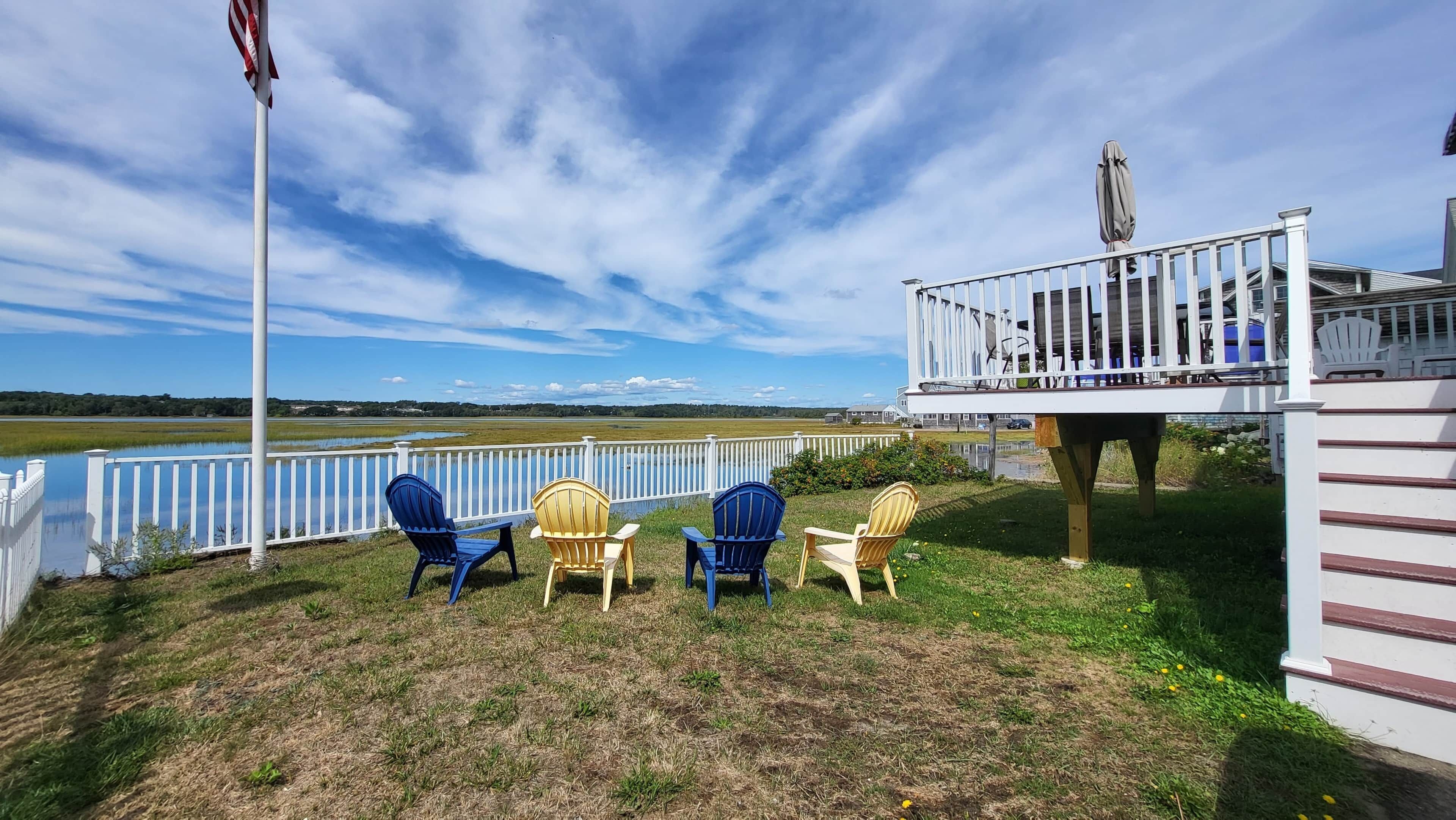 A deck with chairs overlooking a lake, a white fence, and a flagpole.
