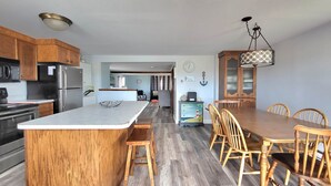 A kitchen with wooden cabinets, a large island, and a dining area with wooden chairs and a table. - Sunset Sanctuary by Wells Beach (Wells)
