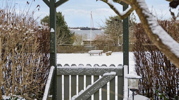 A snow-covered outdoor area with a wooden pergola, a bench, and a view of a body of water. - 4 Star Holiday Home in Sydals (Sydals)