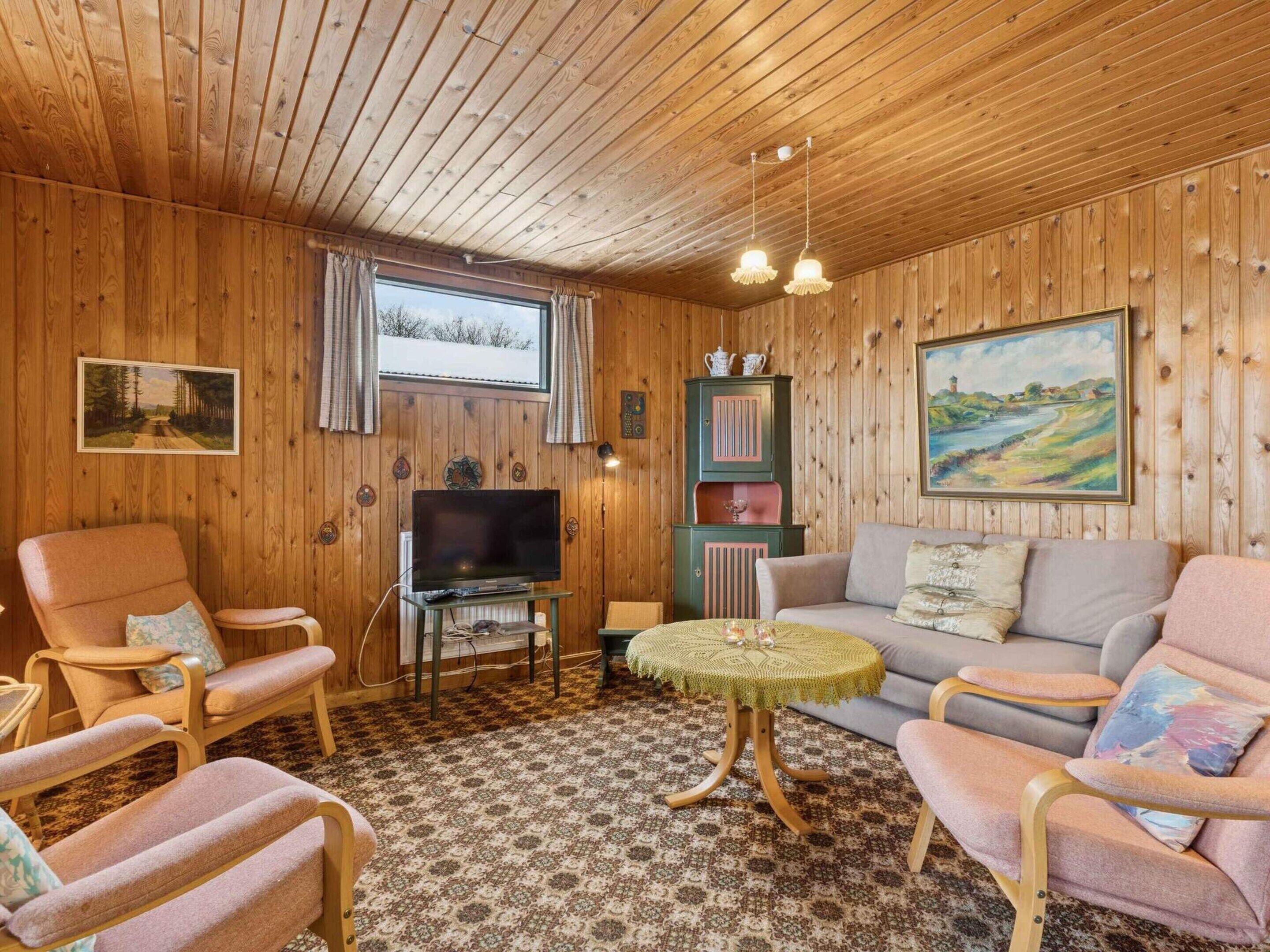 Um quarto acolhedor com paredes de madeira, televisão, sofá e duas poltronas.
