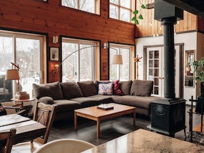 Ein gemütliches Wohnzimmer mit einer Eckcouch, einem Holztisch, einem Kamin und großen Fenstern.