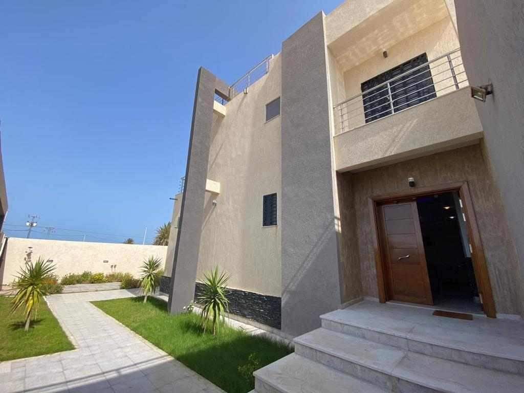 Un bâtiment moderne à la façade plate, doté d’une entrée bien visible et d’un petit espace extérieur agrémenté d’un chemin et de plantes.