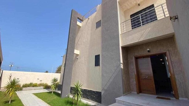 A modern building with a flat facade, a visible entrance, and a small outdoor area with a pathway and plants. - Villa Laguna (Médenine)