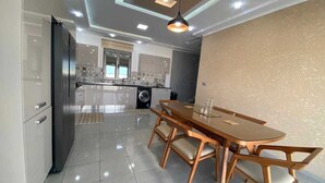 A modern kitchen with a dining area, featuring a large table and chairs, a refrigerator, and a washing machine. - Villa Laguna (Médenine)