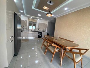 A modern kitchen with a dining area, featuring a large table and chairs, a refrigerator, and a washing machine. - Villa Laguna (Médenine)