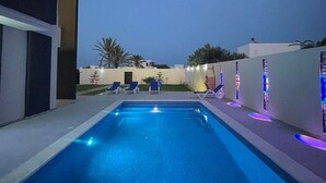 A swimming pool with blue lighting, lounge chairs, and a modern building. - Villa Laguna (Médenine)