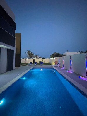 A swimming pool with blue lighting, lounge chairs, and a modern building. - Villa Laguna (Médenine)