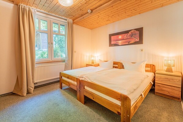 Une chambre à coucher avec un lit en bois, des lampes de chevet, une fenêtre avec des rideaux et un tableau au mur.