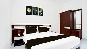 A hotel room with a bed, a nightstand with a vase of flowers, a wardrobe, and a mirror. - Deluxe Moonlit Royal Grand Suite (Aluva)