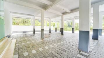 An indoor space with a tiled floor, white pillars, and large windows allowing natural light.
