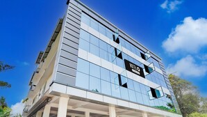 A modern hotel building with a glass facade, a prominent sign, and a covered entrance area. - Deluxe Moonlit Royal Grand Suite (Aluva)