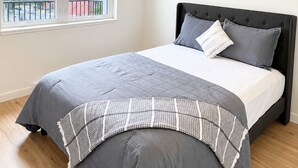A bedroom with a large window, a bed with grey bedding, and a ceiling light fixture. - Top Floor Walk to Beach & Casino (Penticton, BC)