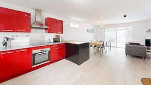 Une cuisine moderne avec des meubles rouges, un îlot central doté d’un plan de travail noir, et un coin repas comprenant une table et des chaises.