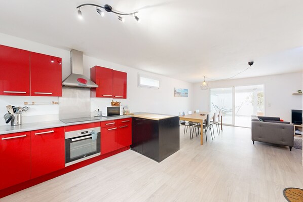A modern kitchen with red cabinets, a black countertop island, and a dining area with a table and chairs.