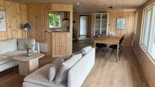 A modern interior with wooden panel walls, a sofa, a dining table with chairs, and a kitchen area. - 4 Star Holiday Home in Ronde (Ronde)