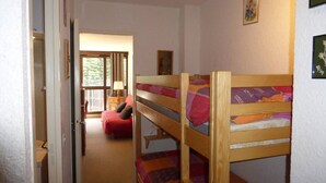 A room with bunk beds, a red sofa, a window with curtains, and a door leading to another room. - Ski-in/ski-out studio with balcony (Enchastrayes)
