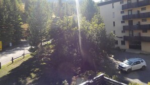 A residential area with a multi-story building, a parked car, and a forested area with mountains in the background. - Ski-in/ski-out studio with balcony (Enchastrayes)