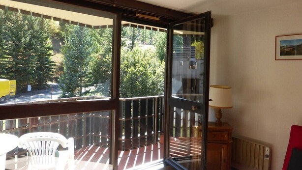 A balcony with a view of trees, a chair, a table, and a lamp. - Ski-in/ski-out studio with balcony (Enchastrayes)