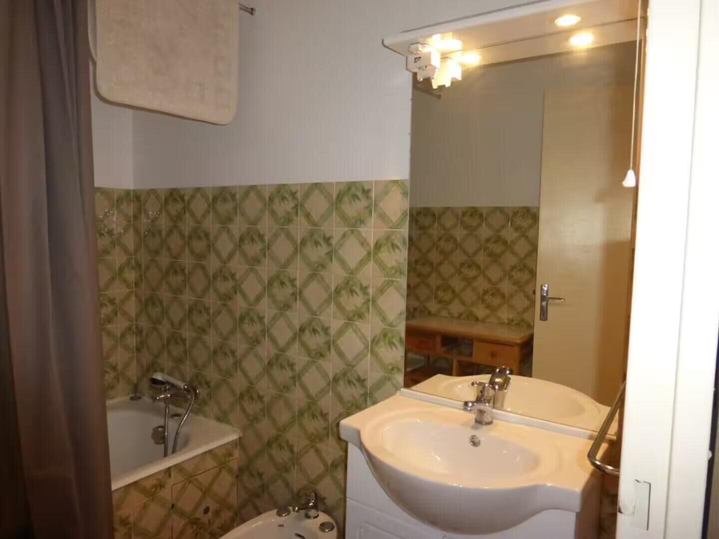 Une salle de bain avec des carreaux décorés, un lavabo, un miroir et une douche.