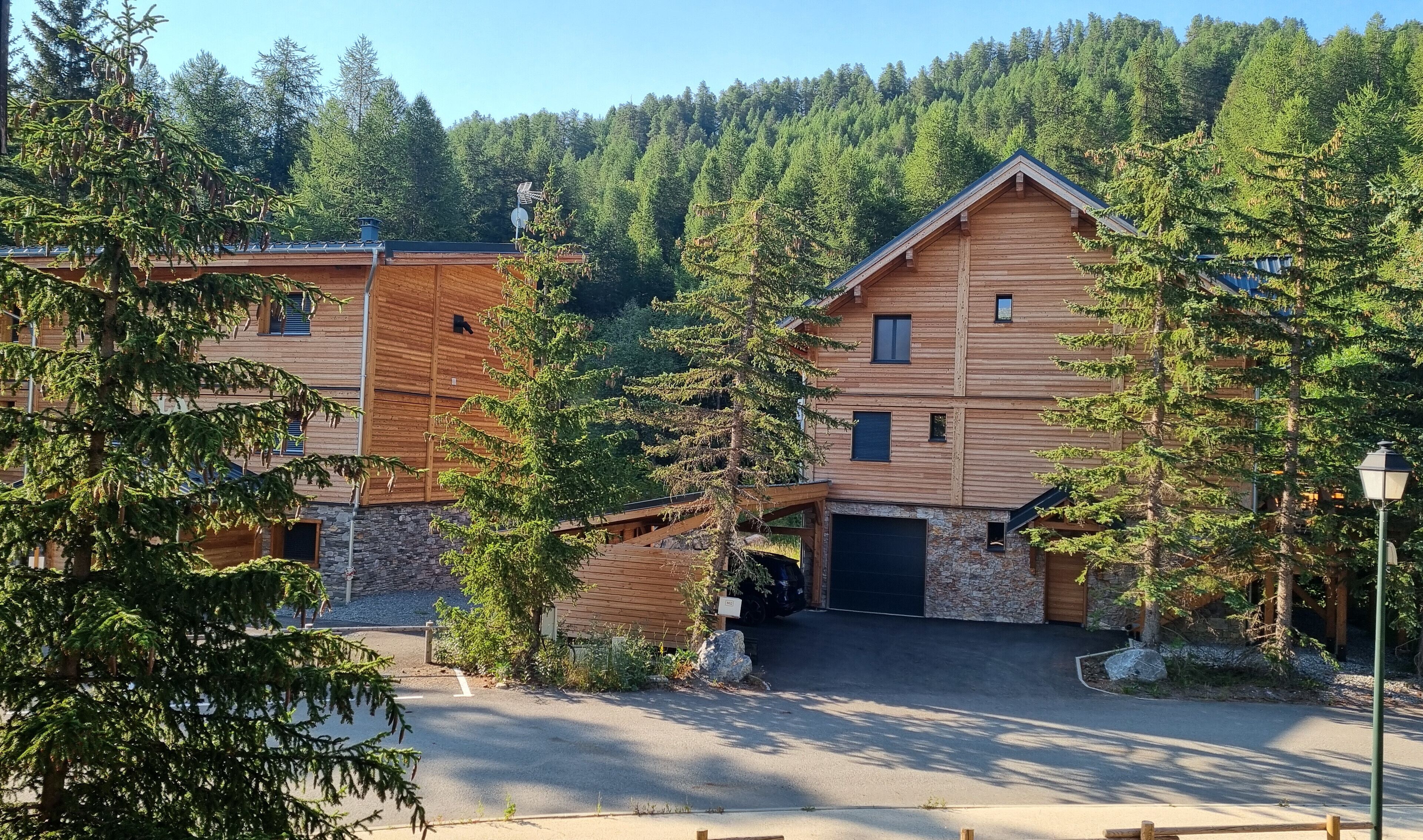 Une cabane en bois à deux étages, avec des fondations en pierre, entourée d’une zone boisée.