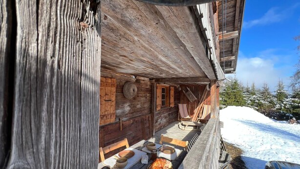 Een houten hut met een veranda, een tafel met fruit en brood, en een besneeerd landschap.