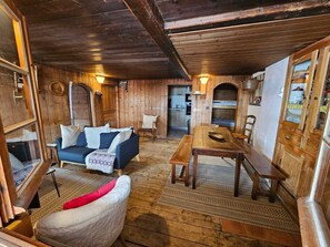 A rustic wooden interior with a sofa, a dining table, and a chair. - Apartment for 8 people –View – Ski-in/ski-out. (La Clusaz)