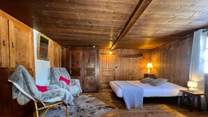 Een houten kamer met een bed, twee stoelen, een lamp en een deur.