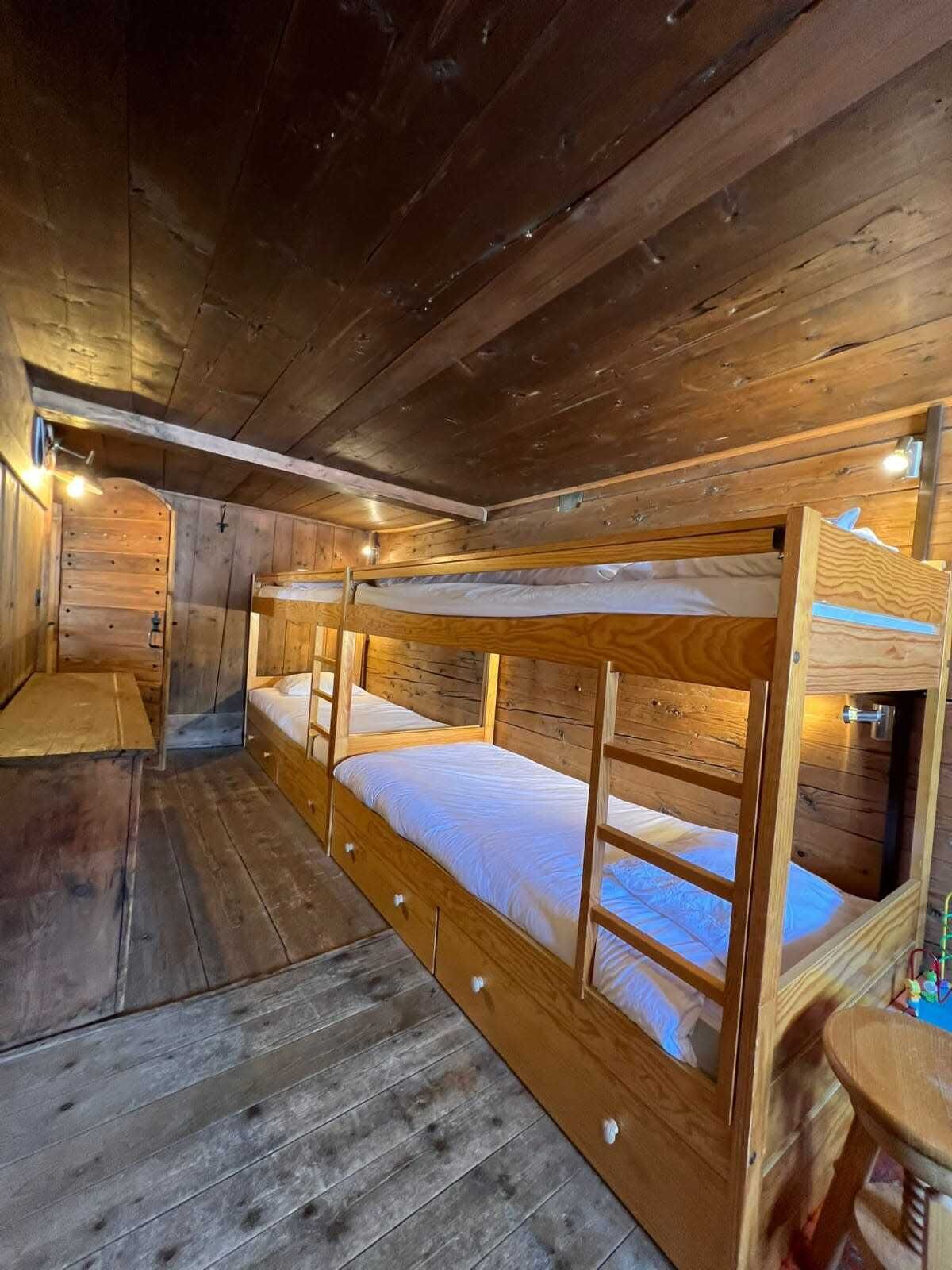 A wooden bunk bed room with a bench and a small table.