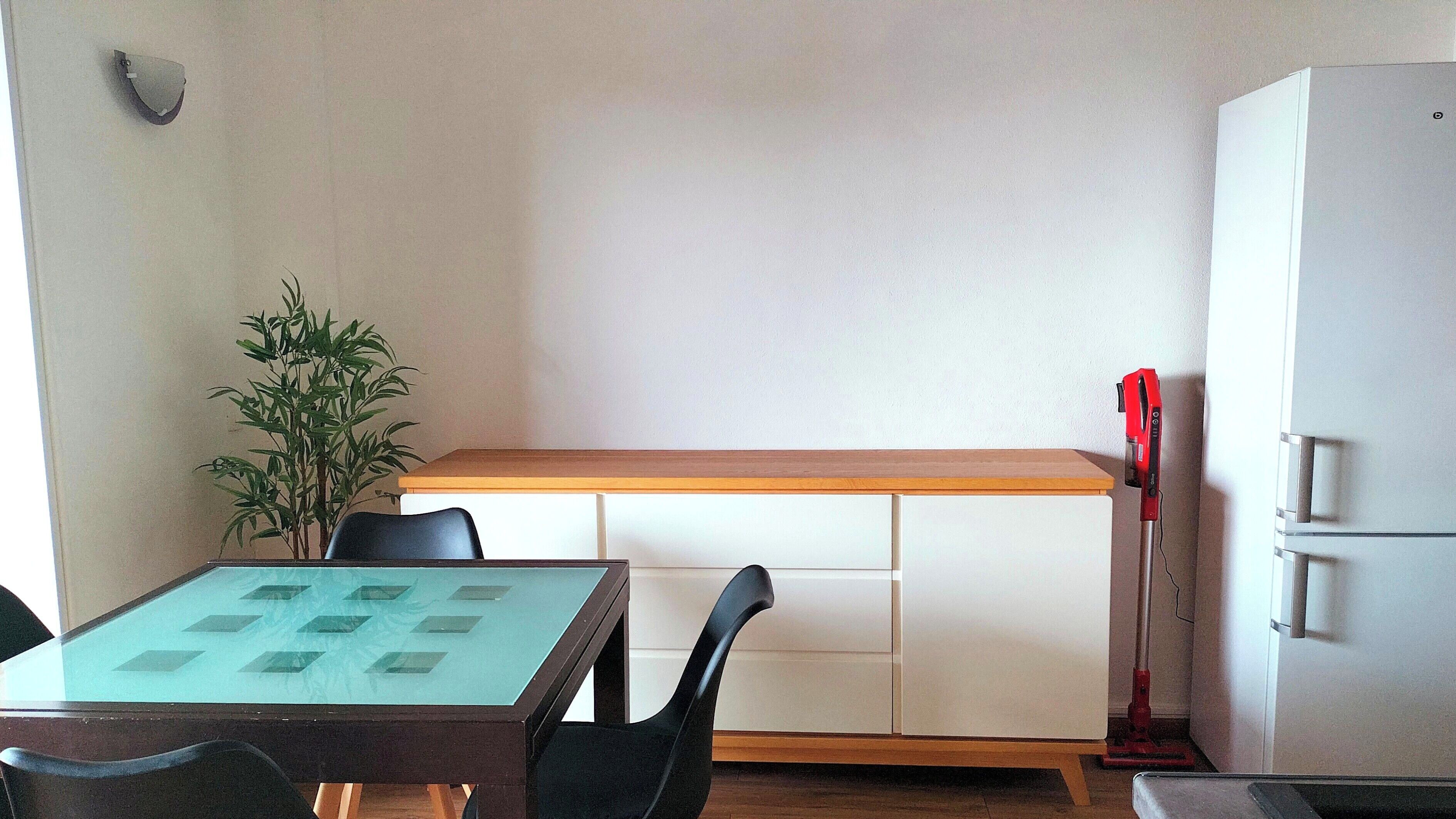 Una pequeña cocina americana con un refrigerador blanco, una encimera de madera, una mesa con cubierta de vidrio y una silla negra.