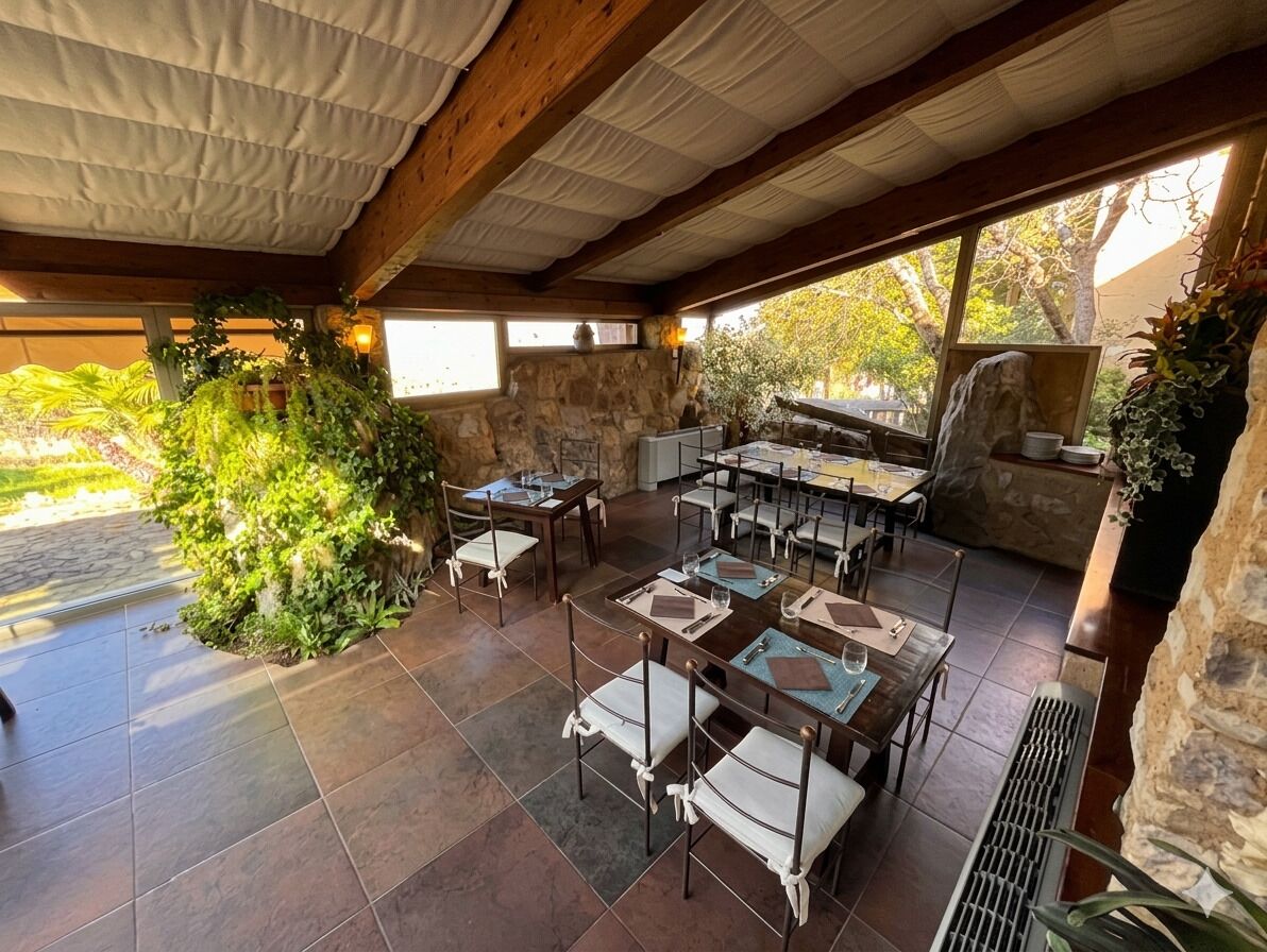 Un patio al aire libre con muros de piedra, vigas de madera y mesas listas para comer.